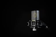 A detailed studio shot of a condenser microphone against a black background, emphasizing modern audio technology.